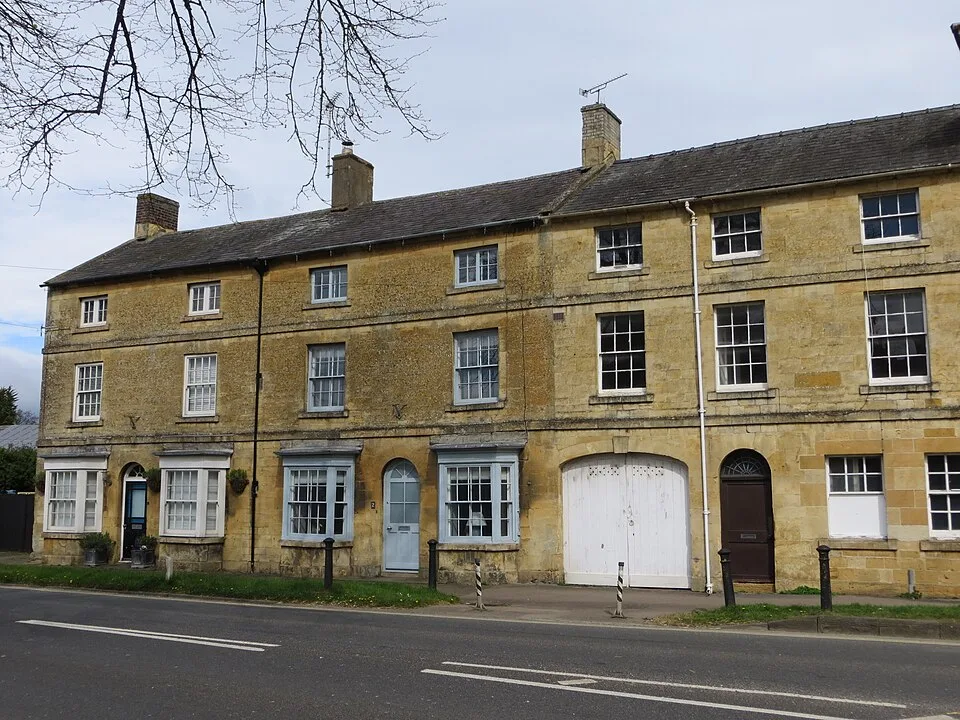 Una schiera di case in pietra calcarea dorata a Moreton-in-Marsh, nei Cotswolds, con i bow-window e le porte azzurro pallido